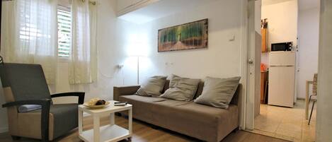 A living room with a sofa, a chair, a small table, and a painting on the wall.