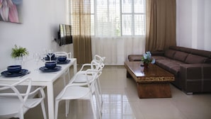 A modern living room with a dining area, featuring a sofa, dining table, chairs, and a TV. - KAV Apartments -Near Assuta Olei Gardom (Tel Aviv)