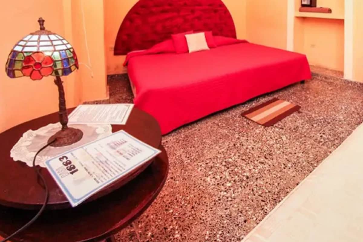 Ein Schlafzimmer mit einem roten Bett, einem kleinen Tisch mit einer Lampe und einem an der Wand befestigten Ventilator.