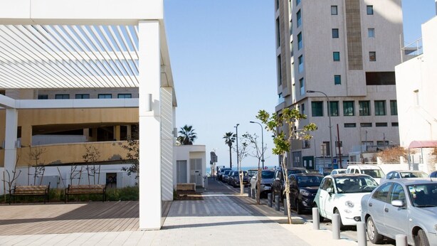 A modern urban street with a row of parked cars, a pedestrian walkway, and tall buildings in the background. - KAV Apartments -HaYarkon St. 30 (Tel Aviv)