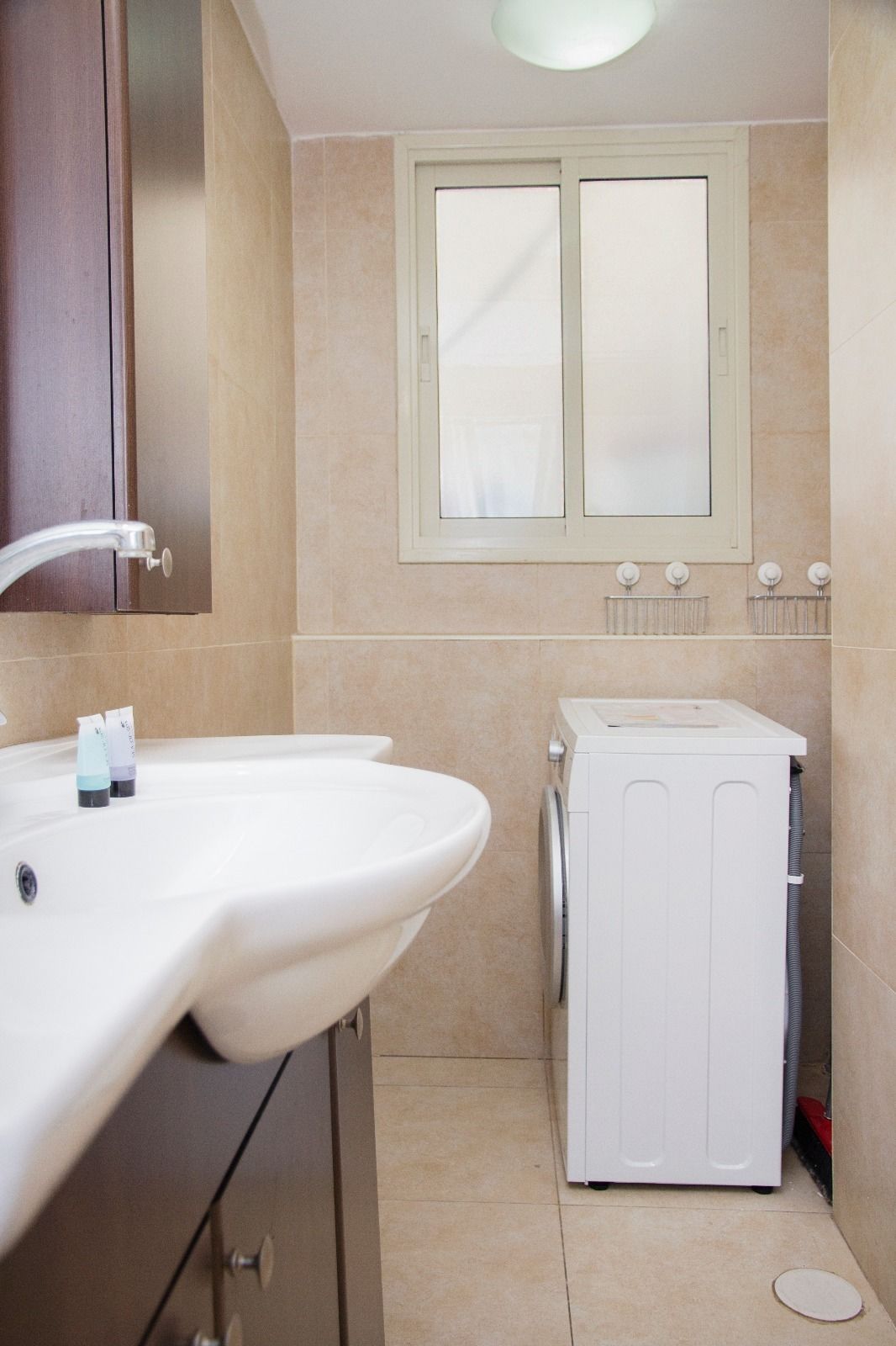 A bathroom with a sink, mirror, window, and a washing machine.