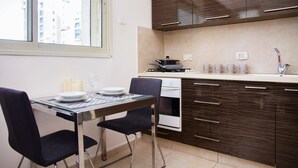 A modern kitchen with dark wood cabinets, a gas stove, and a dining table with chairs. - KAV Apartments -HaYarkon St. 30 (Tel Aviv)