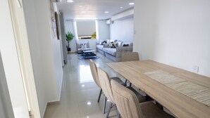 A modern dining area with a long wooden table, beige chairs, and a glass partition. - YalaRent SeaView 3BR APT - Families only (Eilat)