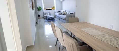 A modern dining area with a long wooden table, beige chairs, and a glass partition.