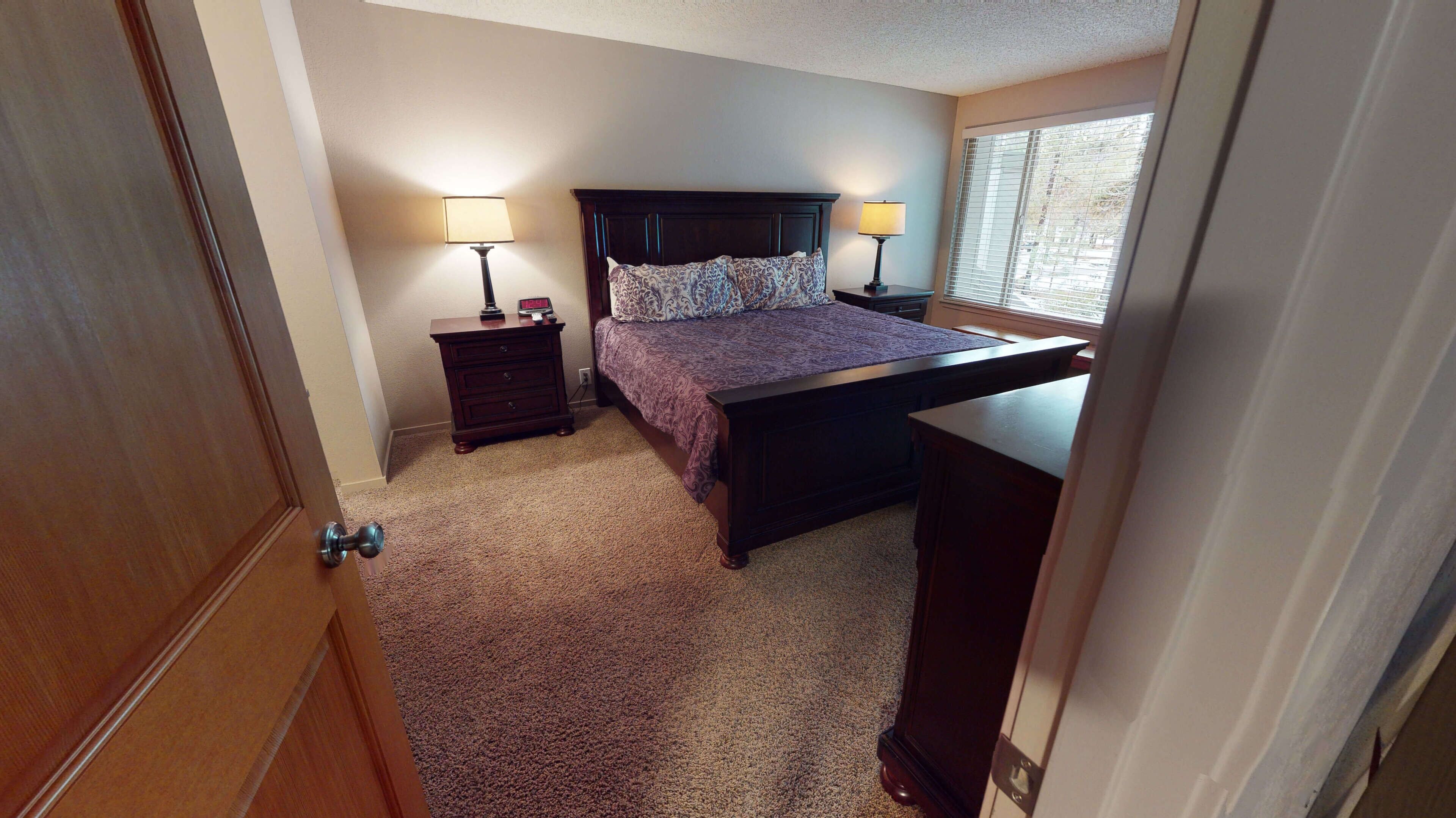 A bedroom with a bed, two bedside tables with lamps, a dresser, and a window with blinds.