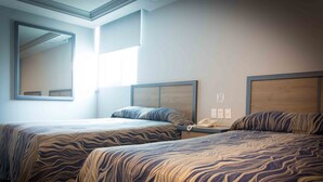 Habitación de hotel con dos camas, cada una con cabecero y teléfono en la mesita de noche.