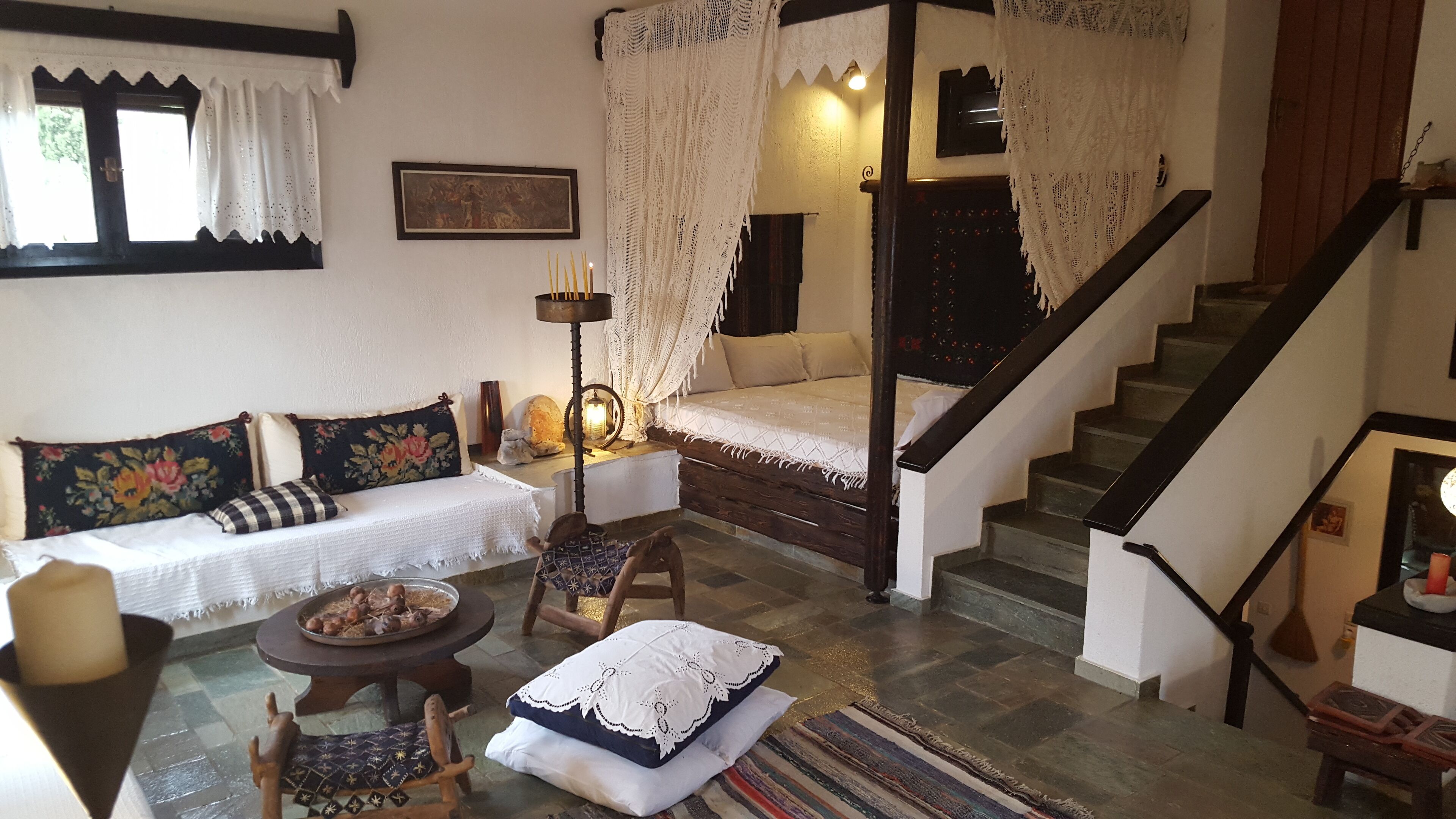 A cozy living room with a sofa, a small table with a bowl of nuts, a chair, a wooden bench, and a staircase leading to an upper floor.