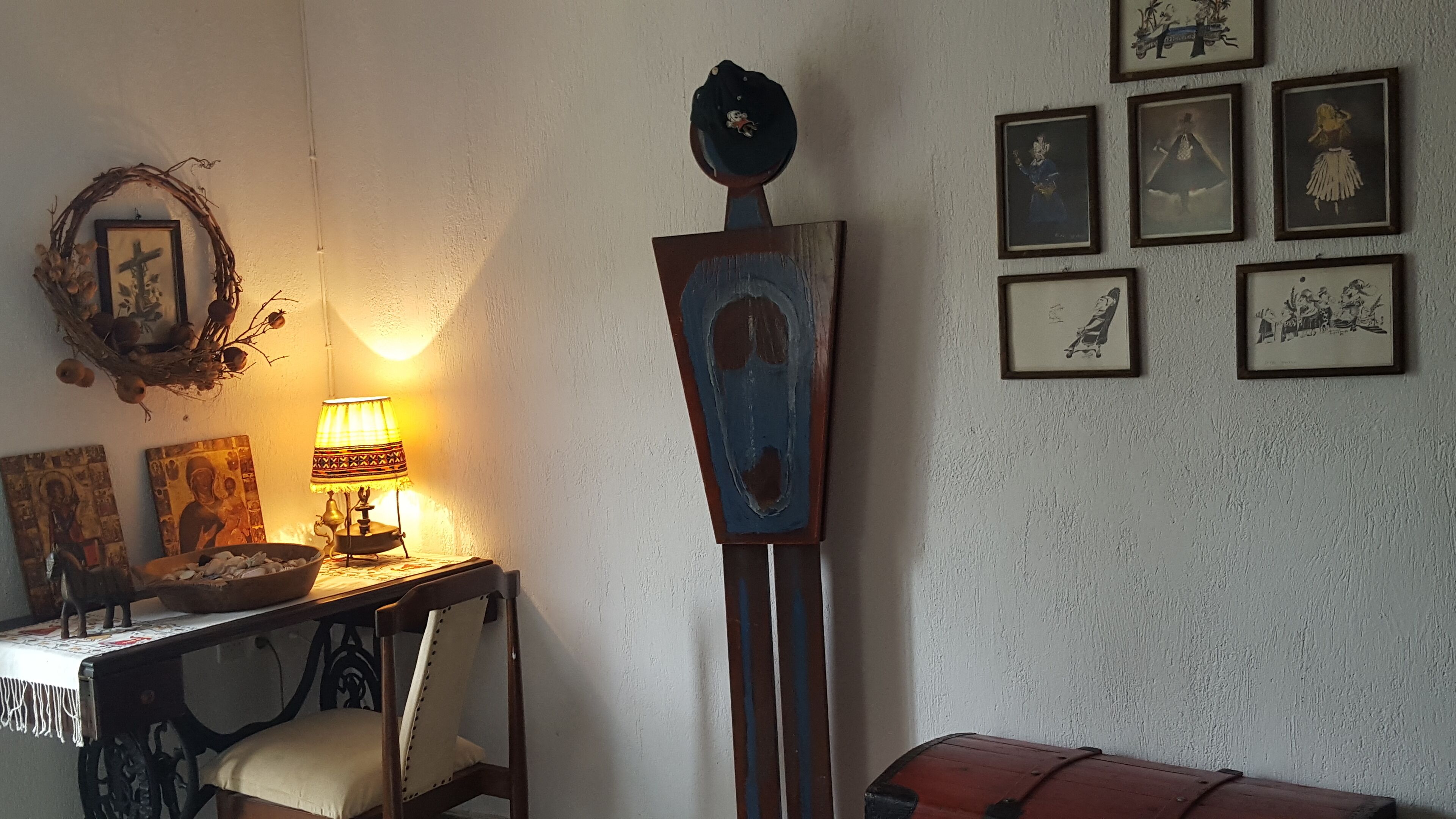 Ett rum med ett skrivbord, en stol, en lampa, en hylla som är monterad på väggen och flera inramade tavlor.