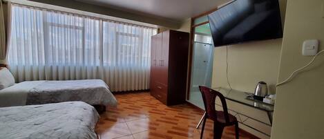Una habitación con dos camas, un escritorio con silla, televisión y armario.
