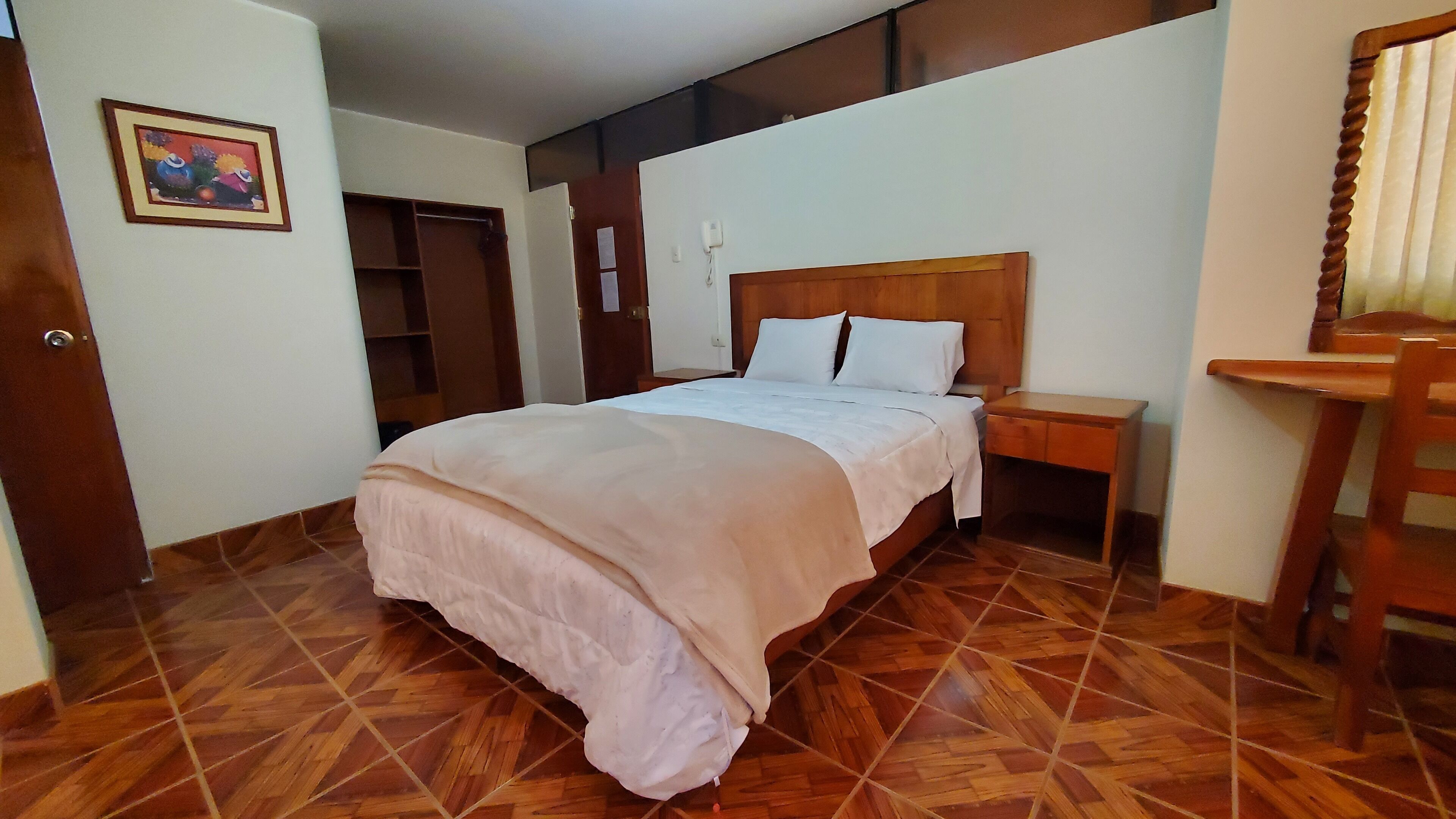 A hotel room with a wooden floor, a bed with white bedding, a wooden nightstand, and a wooden chair.