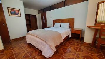 A hotel room with a wooden floor, a bed with white bedding, a wooden nightstand, and a wooden chair.