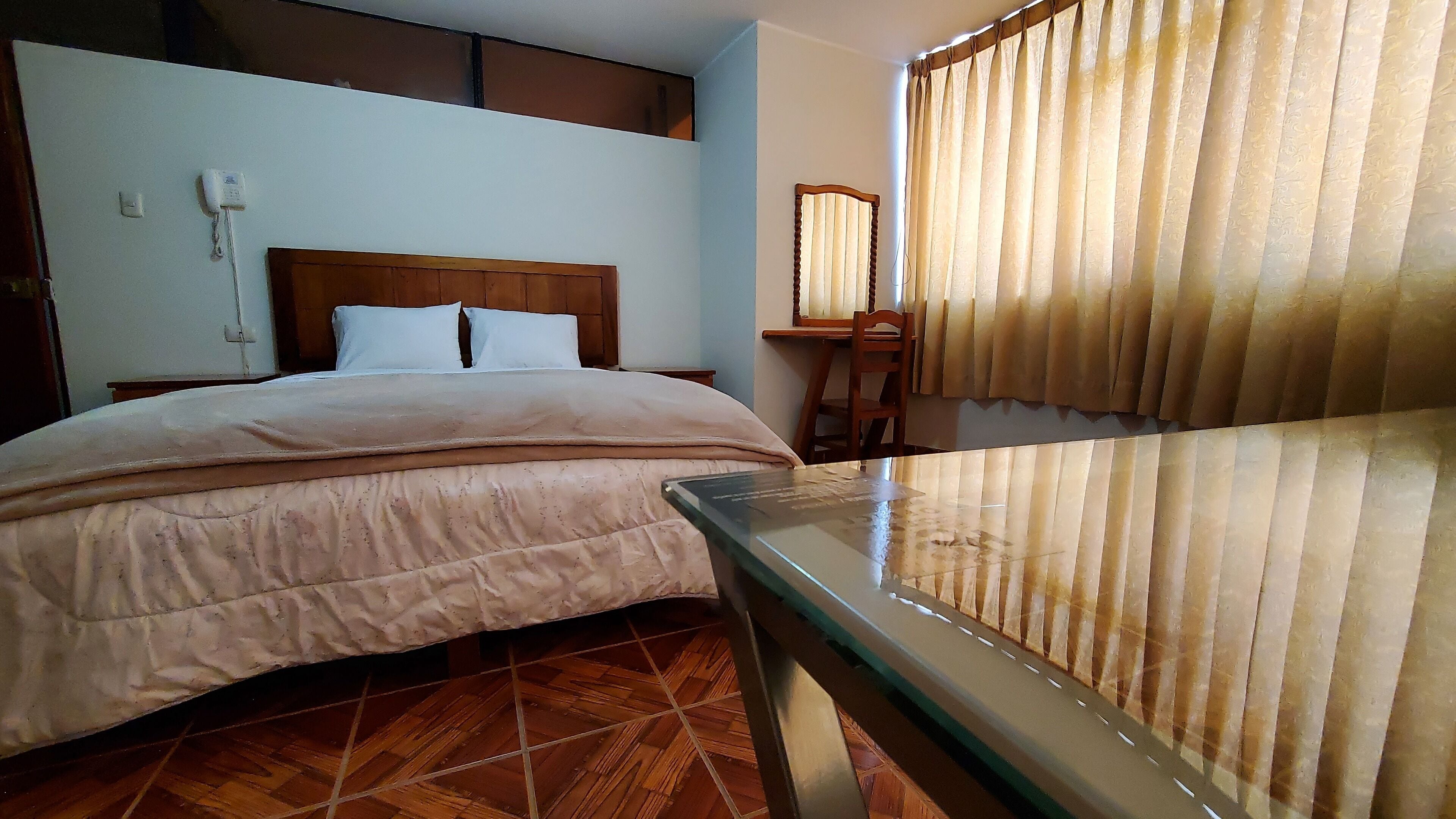Una camera d'albergo con un letto, una scrivania e una finestra con tende.