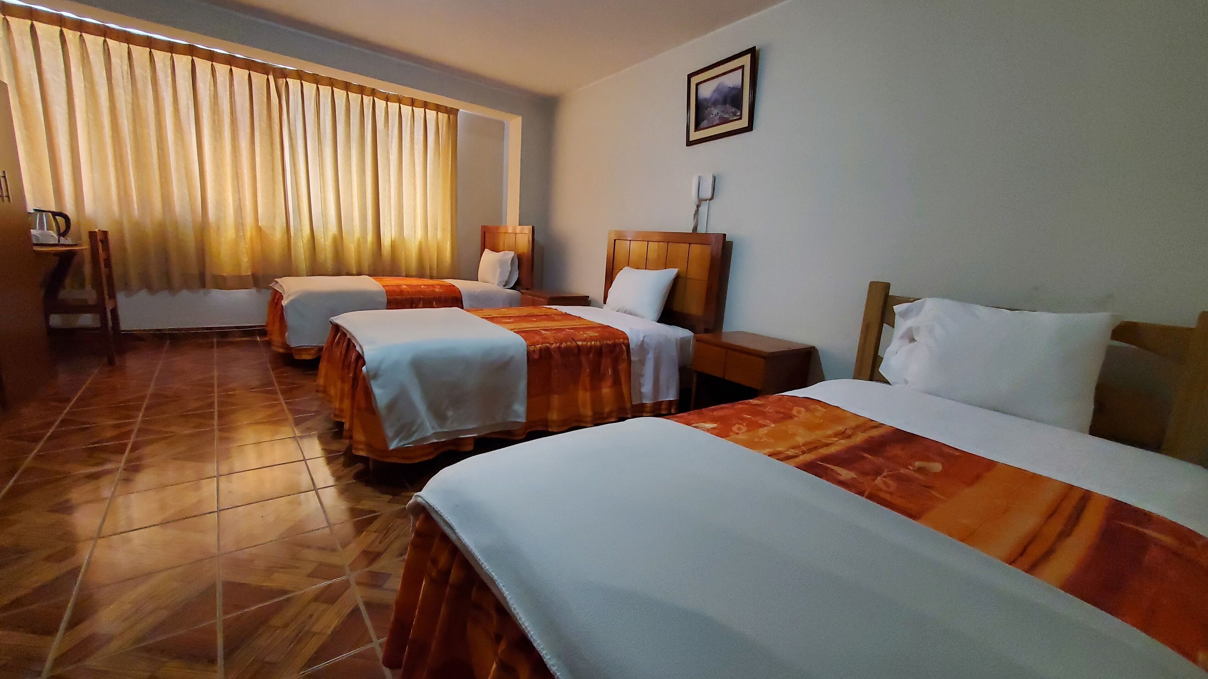A hotel room with three beds, a wooden headboard, a nightstand, a lamp, and a framed picture on the wall.