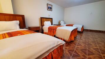 Ein Hotelzimmer mit drei Betten, einem hölzernen Kopfteil, einem Nachttisch, einem kleinen Schreibtisch, einem Telefon und einem Bild an der Wand.