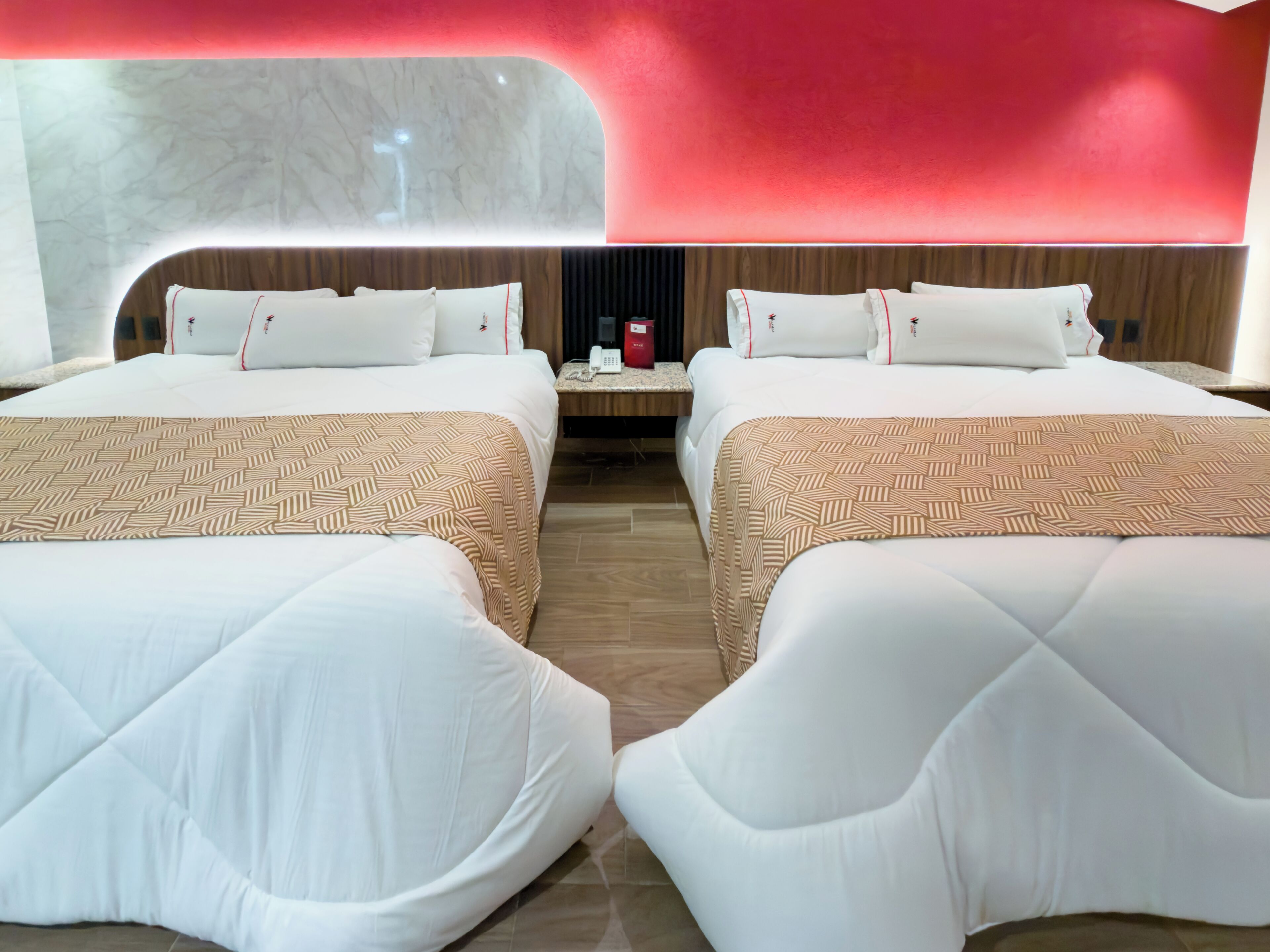 Habitación de hotel con dos camas, pared de mármol y una pared de acento roja.