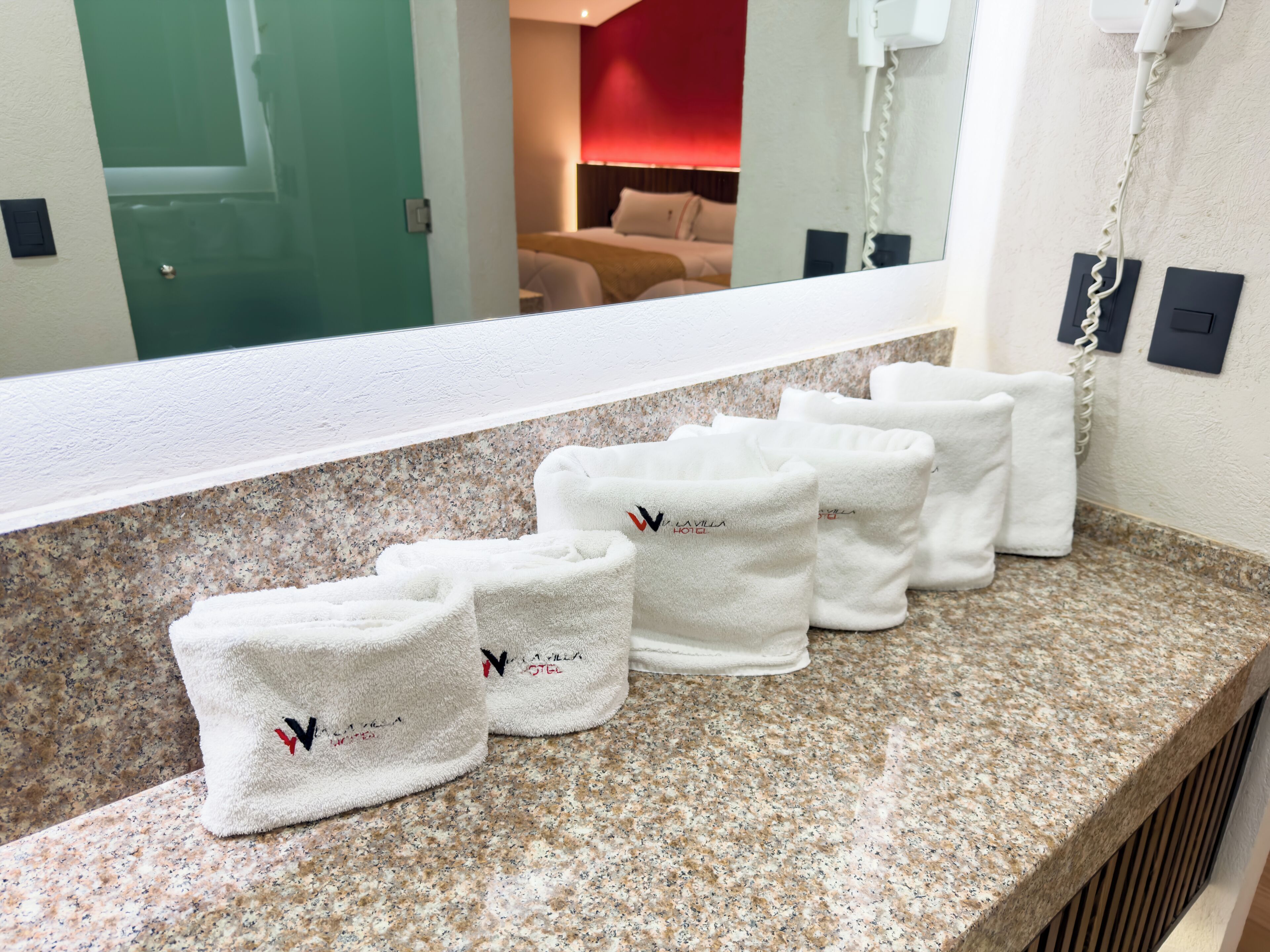 Casa de banho de hotel com bancada de granito, um espelho e várias toalhas brancas com um logótipo.