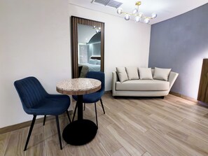 Moderni olohuone, jossa on pyöreä pöytä, kaksi sinistä tuolia, beige sohva ja kattovalaisin.
