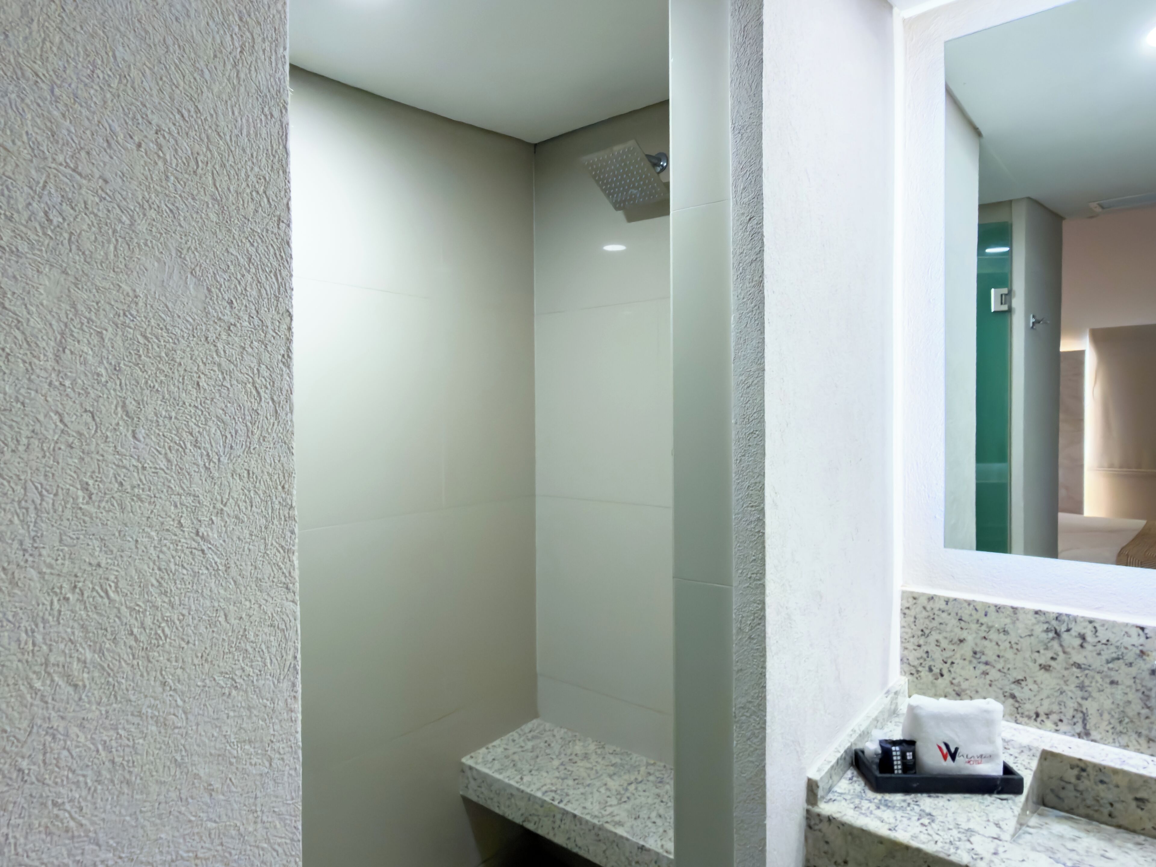 Un baño con ducha, un lavabo con encimera de m ármol y un espejo que refleja una puerta verde.