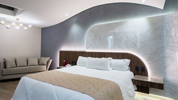 Une chambre d’hôtel moderne dotée d’un grand lit, d’un canapé, d’une table de chevet et d’une tête de lit au design incurvé et original.