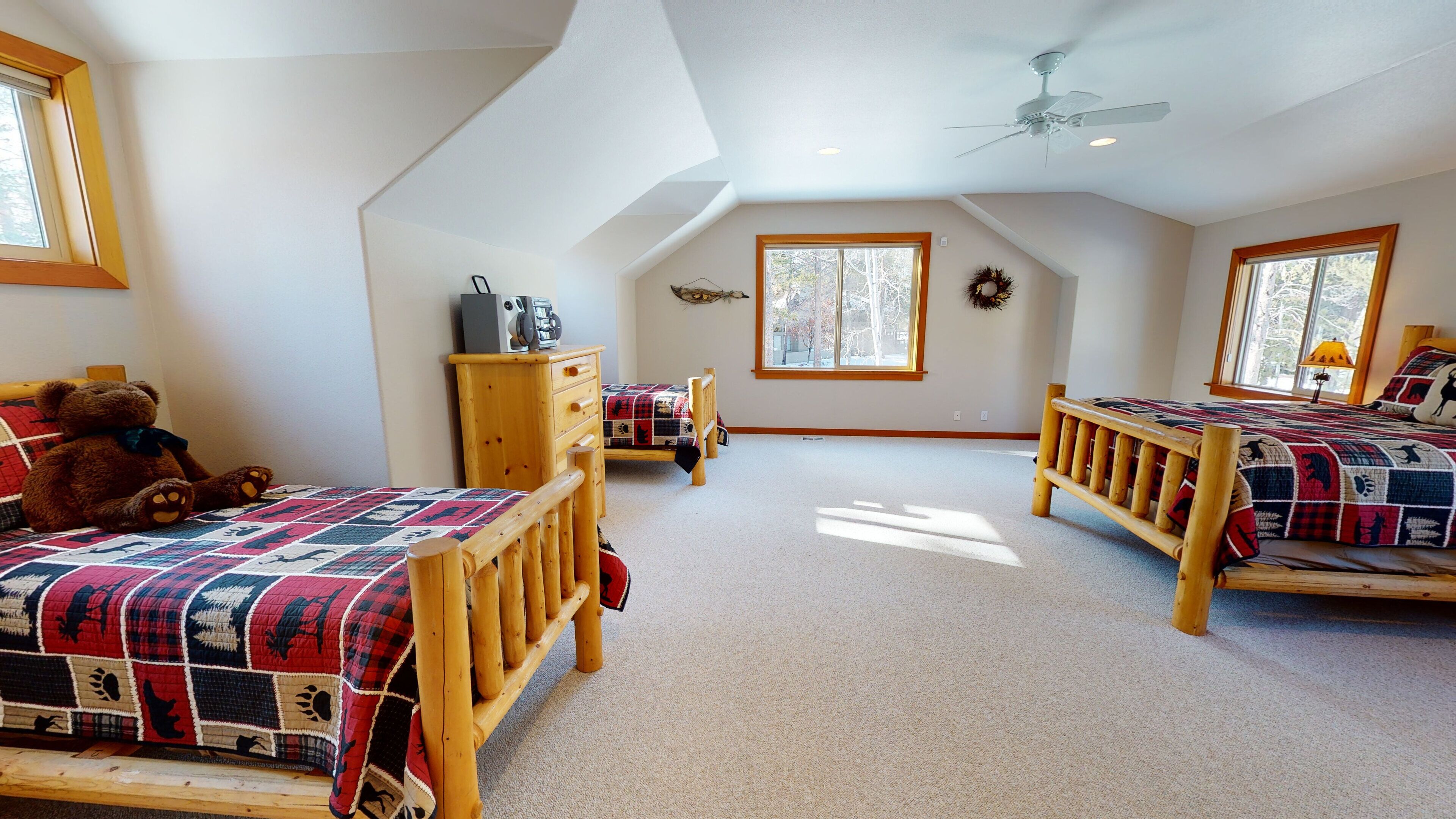 A spacious attic bedroom with two wooden beds, a ceiling fan, and large windows.