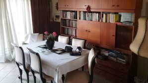 Comedor con una mesa dispuesta para cuatro personas, rodeada de sillas. A la derecha, una estantería llena de libros.