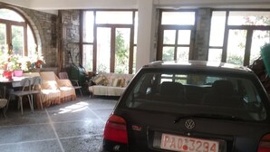 Un coche estacionado dentro de un edificio con grandes ventanales, una pared de piedra y un suelo de baldosas.