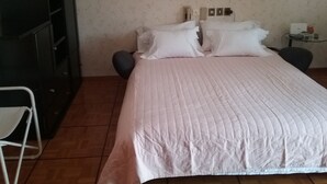 Un dormitorio con cama, una silla, una mesita y un espejo en la pared.