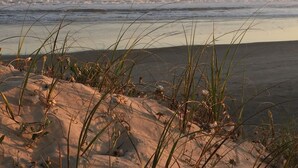 A beach with sand dunes and grass in the foreground, leading to the ocean. - Complejo Casas del Mirador (Puimayen)