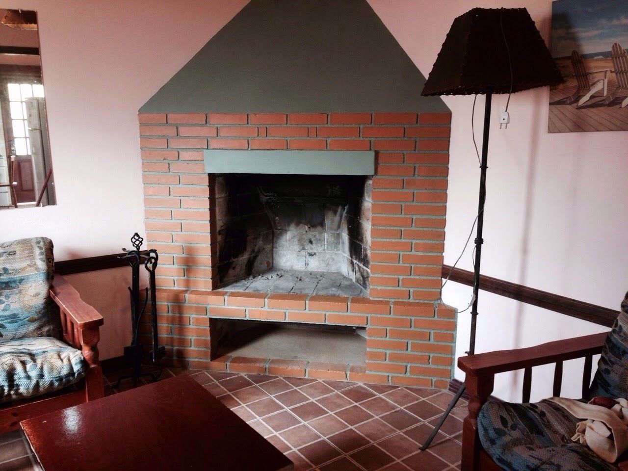 Una chimenea de ladrillo con repisa, un banco de madera y una silla en una habitación con techo inclinado y suelo de madera.