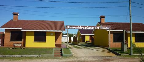 Una hilera de edificios de estilo motel en tonos amarillo y marrón, con un letrero que dice "Bienvenidos a Casas del Mirador".