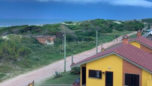 A yellow building with a red roof, a dirt path, and a view of the ocean and hills. - Complejo Casas del Mirador (Puimayen)