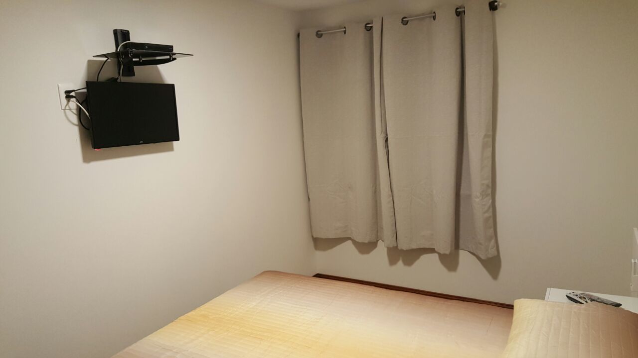 A room with a bed, a mounted projector, and a curtain.