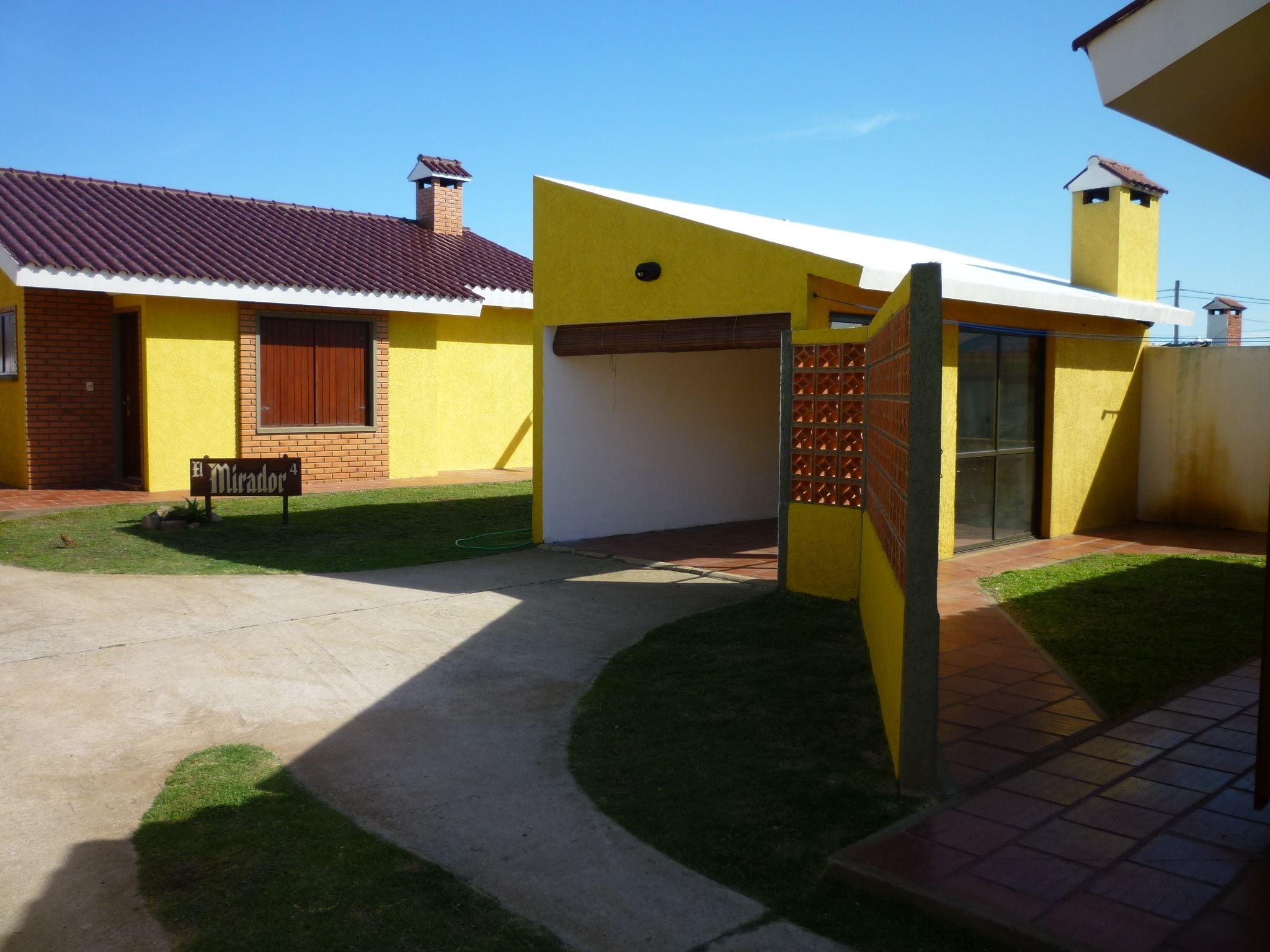 A yellow building with a red-tiled roof, a small garden, and a paved walkway.