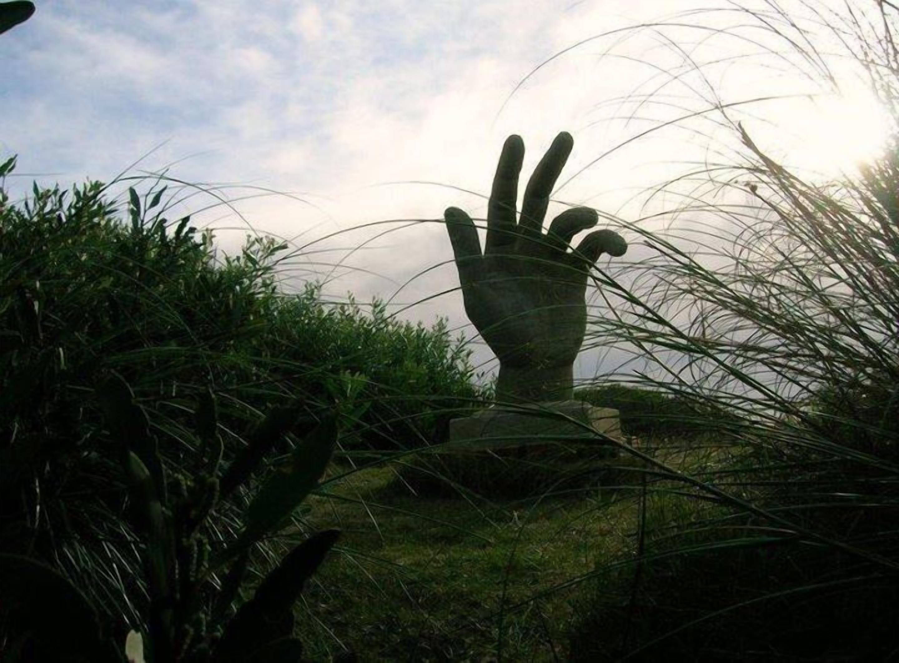 A sculpture of a hand amidst greenery.