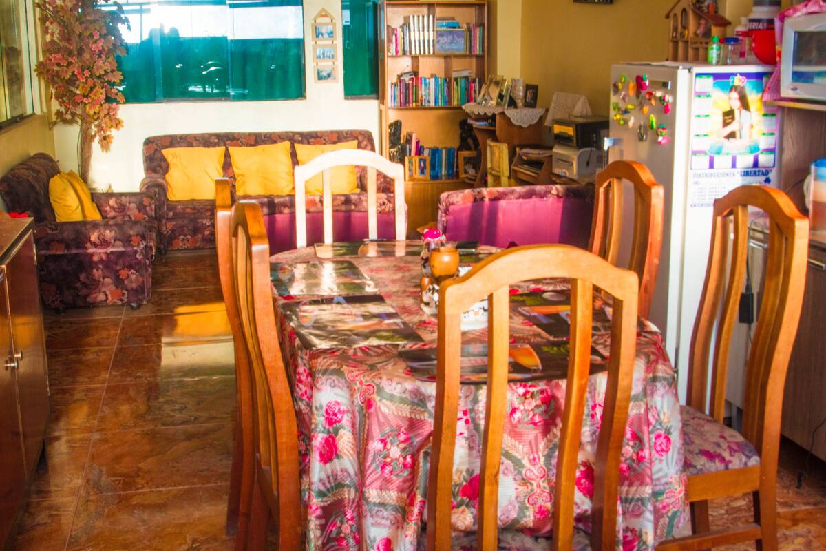 Un comedor con una mesa cubierta por un mantel floral, rodeada de sillas de madera.