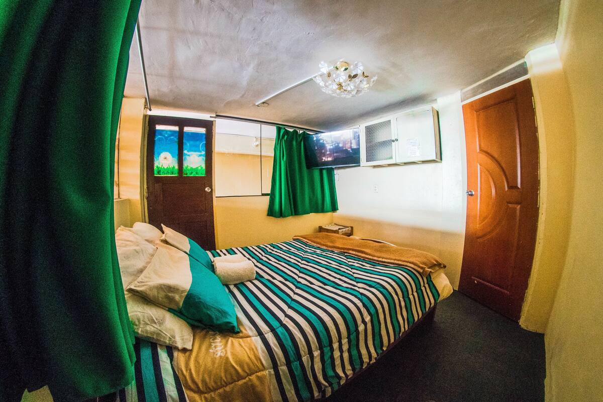 Una habitación con cama, televisión, puerta y ventana con cortinas.