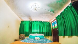 Un dormitorio con una cama, cortinas verdes, una araña y un cabecero de madera.