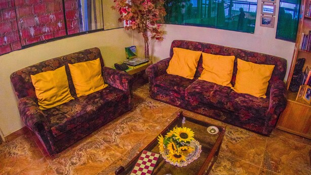 Una sala de estar con dos sofás estampados, una mesa de centro con un tablero de ajedrez y un ventanal con vistas a un edificio.