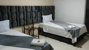 A hotel room with two beds, a padded headboard, and a small table.