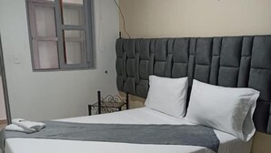A bedroom with a large bed, a headboard, a window, and a nightstand. - Hotel Empresarial  (Pereira)