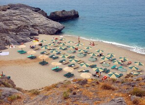 A beach with numerous umbrellas and lounge chairs, rocky terrain, and a view of the sea. - Calergi 16 - Boutique Resort Studio: Pool/Rooftop for Coffee in Sunset/Rethymno (Ατσιπόπουλο)