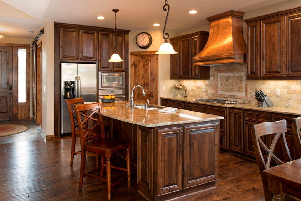 A kitchen with wooden cabinets, a stainless steel refrigerator, a large island with a sink, and pendant lighting.