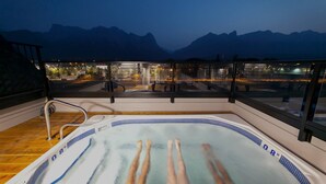 A hot tub on a balcony with a view of mountains and a cityscape at night. - Basecamp Resorts Canmore, Basecamp Bargain Suite (Canmore)