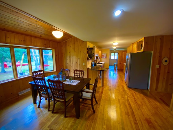 A wooden cabin interior with a dining area, kitchen, and large windows. - Quiet, isolated, beautiful home (Crivitz)