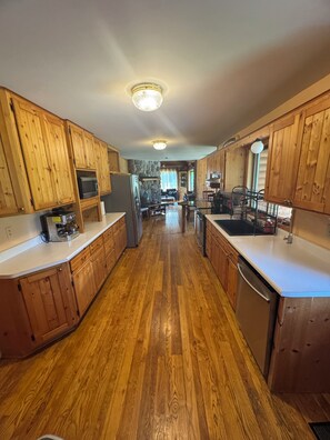 A kitchen with wooden cabinets, a central island, and a view into the living area. - Quiet, isolated, beautiful home (Crivitz)