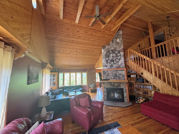 A wooden interior with a stone fireplace, a staircase, and a seating area with leather sofas.