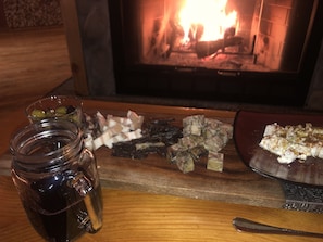 A wooden table with a glass jar of dark liquid, a plate with food, and a fireplace in the background. - Quiet, isolated, beautiful home (Crivitz)