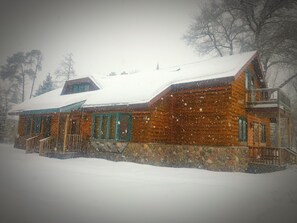 A wooden cabin with a snow-covered roof, a stone foundation, and a balcony on the upper floor. - Quiet, isolated, beautiful home (Crivitz)