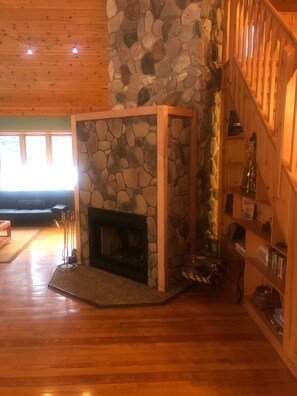 A stone fireplace with a wooden mantel, a wooden staircase to the right, and a wooden floor. - Quiet, isolated, beautiful home (Crivitz)