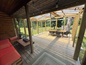 A covered outdoor deck with a wooden table and chairs, a cushioned bench, and a grill. - Quiet, isolated, beautiful home (Crivitz)